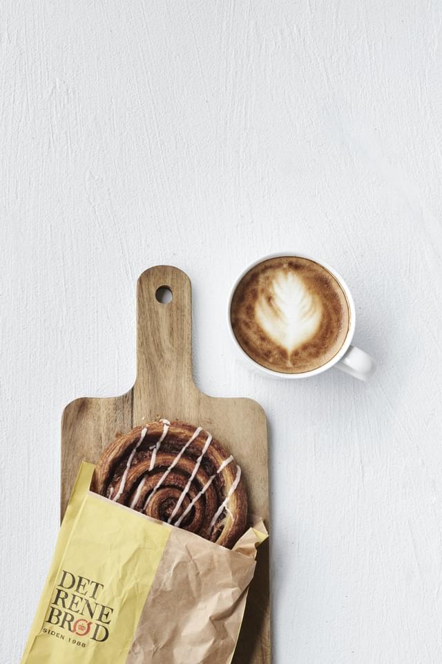 Kanelsnegl på skærebrædt og en kop kaffe